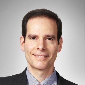 A male with brown hair, a grey background, he's in a suit