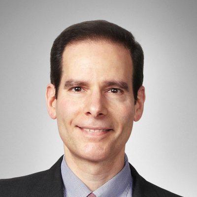 A male with brown hair, a grey background, he's in a suit