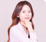 Hannah in in a white blazer and her hand on her chin. She has dark, long hair. 