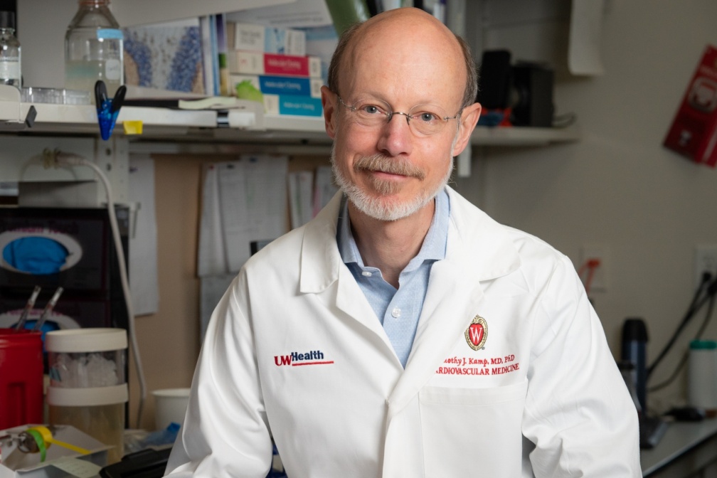 Tim Kamp in a white lab coat with lab materials in the background